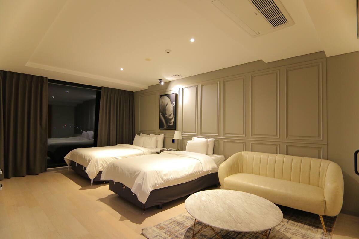 Habitación de hotel con dos camas, un sofá, una mesa de centro redonda y un cuadro grande en la pared.