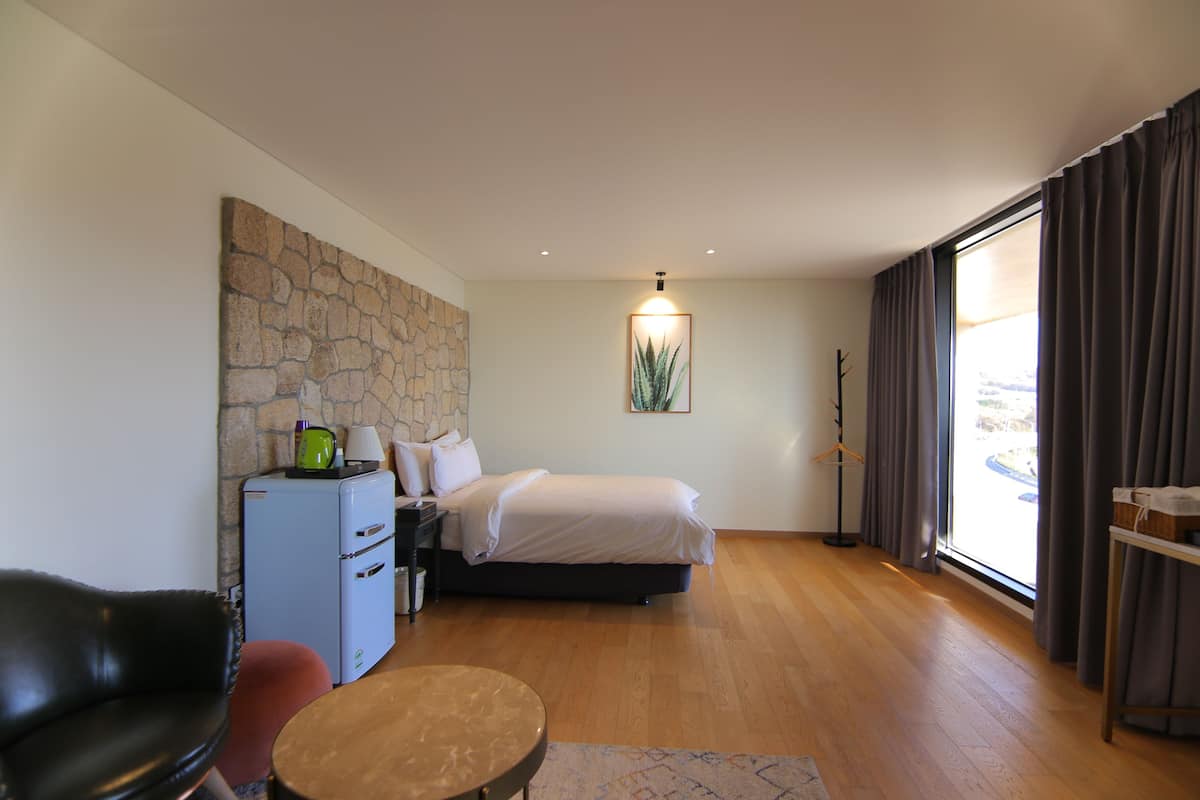 Una habitación de hotel moderna con una pared de acento de piedra, una cama, un escritorio, una silla y un ventanal con cortinas.