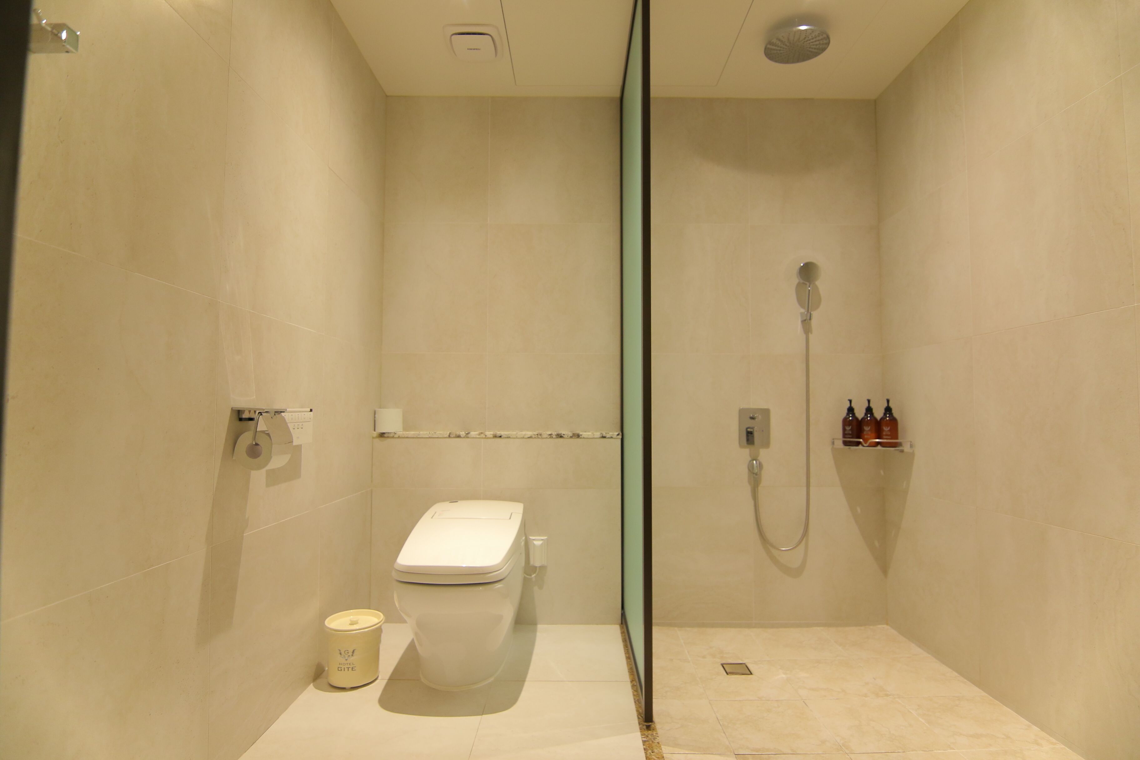 A modern bathroom with a glass-enclosed shower, a toilet, and a small shelf with toiletries.