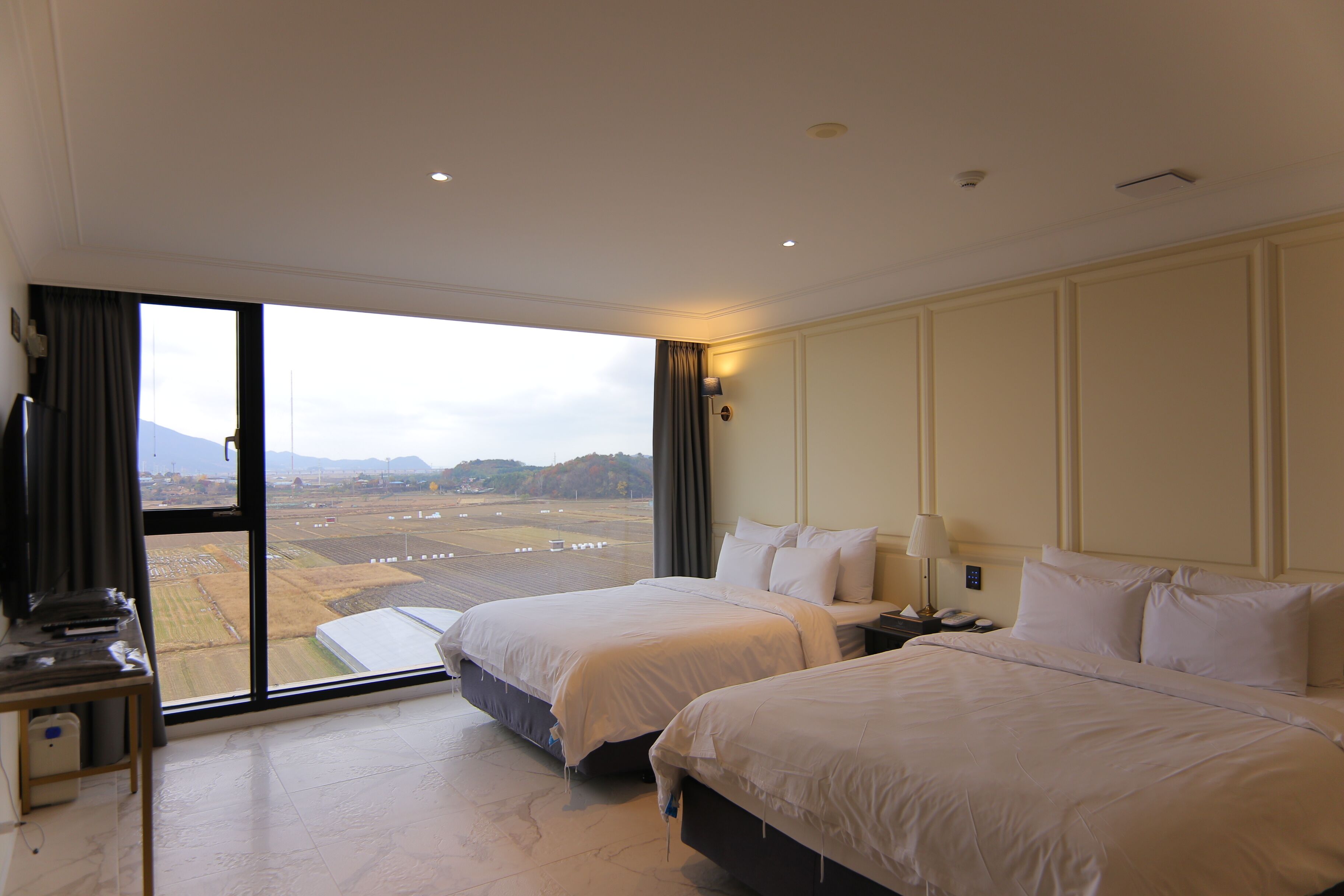 A hotel room with two beds, a desk, and a large window offering a view of a landscape.