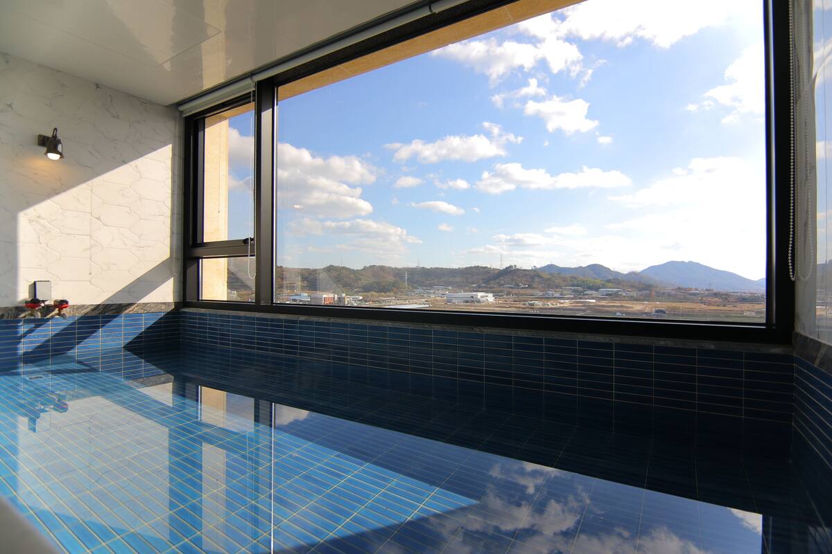 Una piscina interior con un ventanal grande que ofrece vistas a un paisaje lejano y montañas.