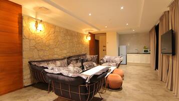 Een moderne woonkamer met een accentmuur van steen, een zithoek, een eettafel en een keuken in de achtergrond.