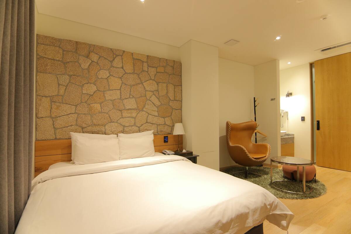 Habitación de hotel con una cama grande, una pared de piedra, una puerta de madera, una silla y una mesita.