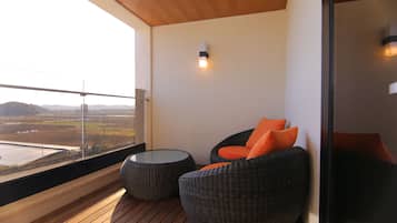A balcony with wicker chairs, a glass table, and a view of a field.