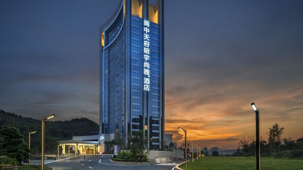 A modern high-rise hotel with a prominent vertical sign, a well-lit entrance, and a surrounding landscaped area. - Galaxy Minyoun Langzhong Tianfu Hotel (Nanchong)