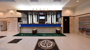 Ein Hotel-Rezeptionsbereich mit einem Schild mit der Aufschrift 'FRONT', einer digitalen Anzeige, einem Empfangstresen, einer Uhr und einem grünen Teppich mit der Webseite des Hotels.