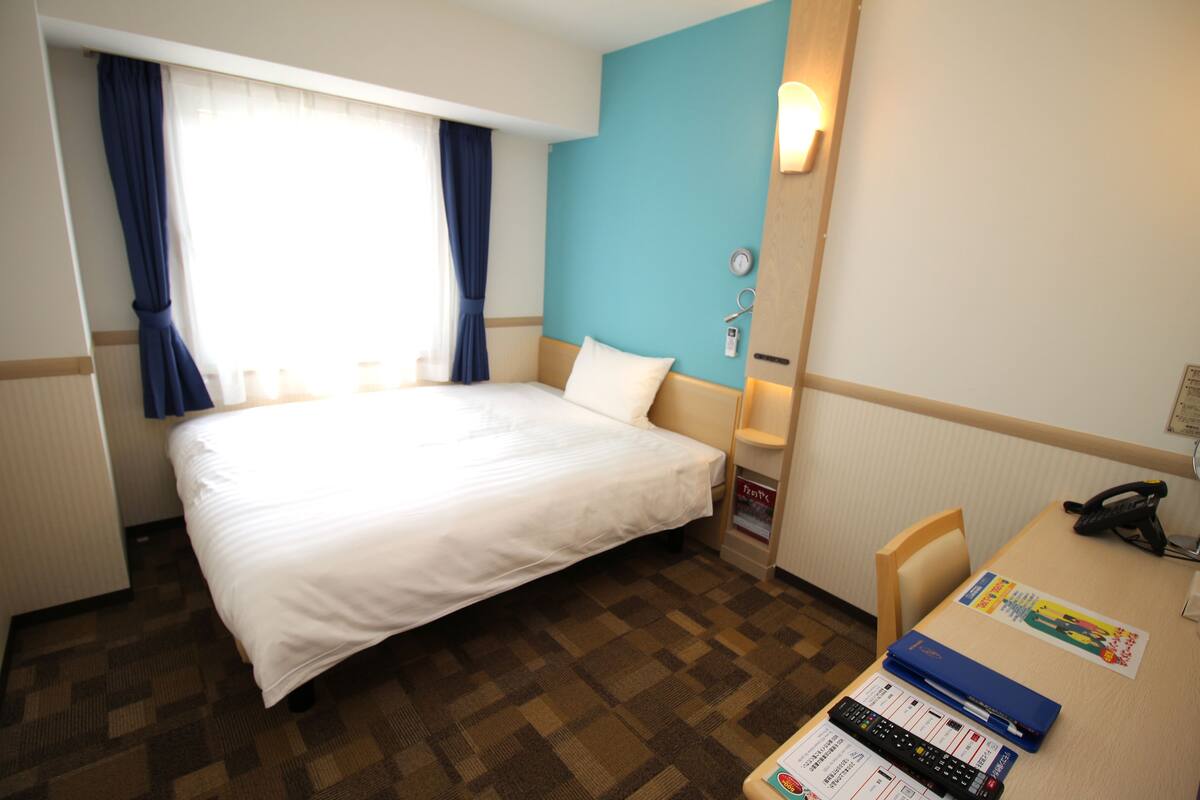 Une chambre d’hôtel avec un grand lit, un bureau avec un téléphone et une fenêtre avec des rideaux.