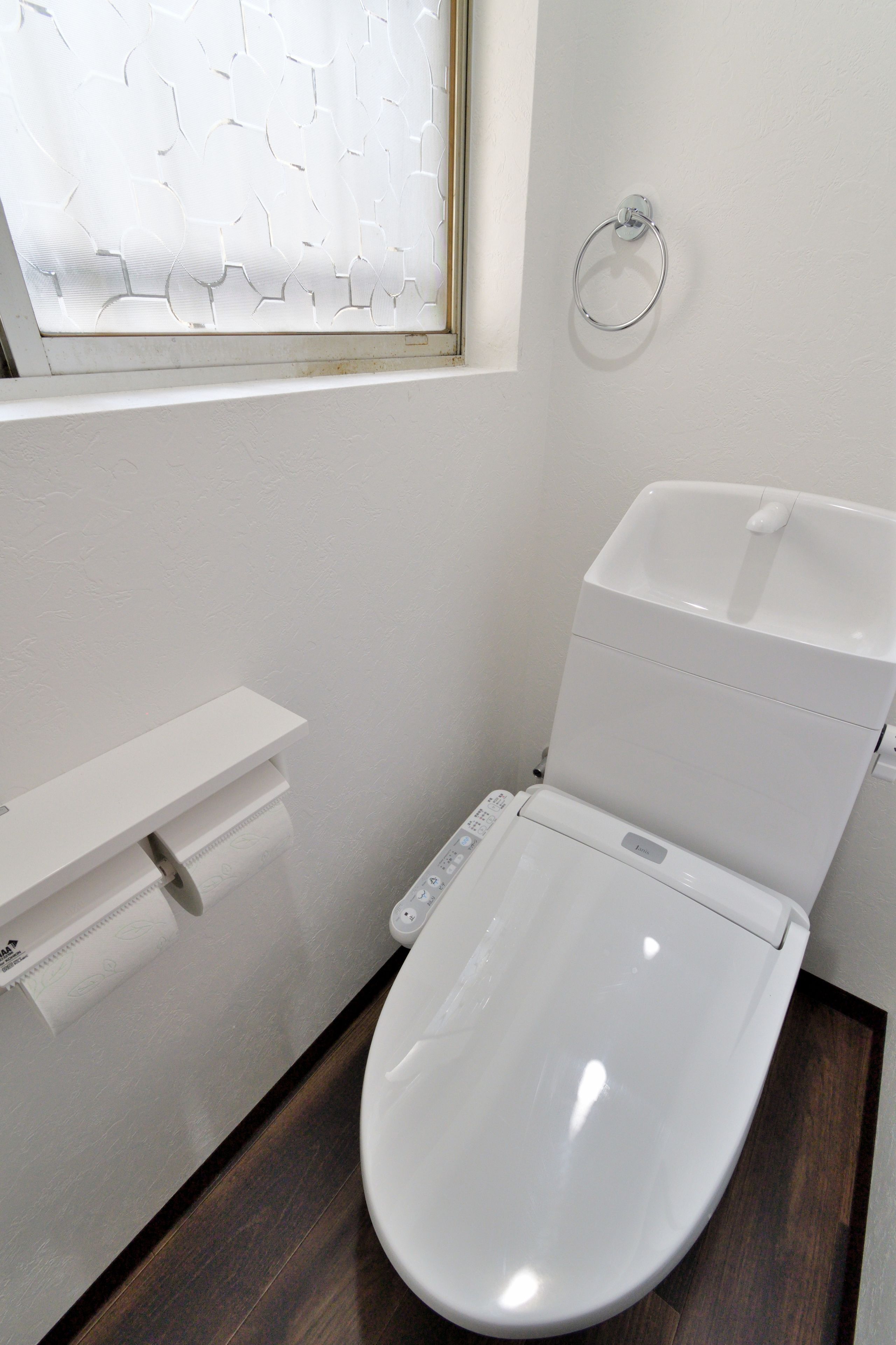 Une salle de bain moderne avec des toilettes blanches, un plancher en bois et une fenêtre à verre dépoli.