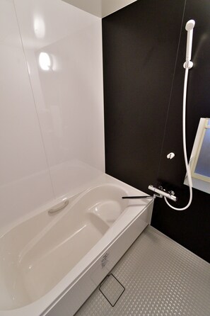 A modern bathroom with a white bathtub, a handheld showerhead, and a wall-mounted faucet. - Machi de kurasu Tengachaya-1 (Osaka)