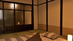A traditional Japanese-style room with tatami flooring, a low bed with a pillow, and a shoji screen. - Machi de kurasu Tengachaya-1 (Osaka)