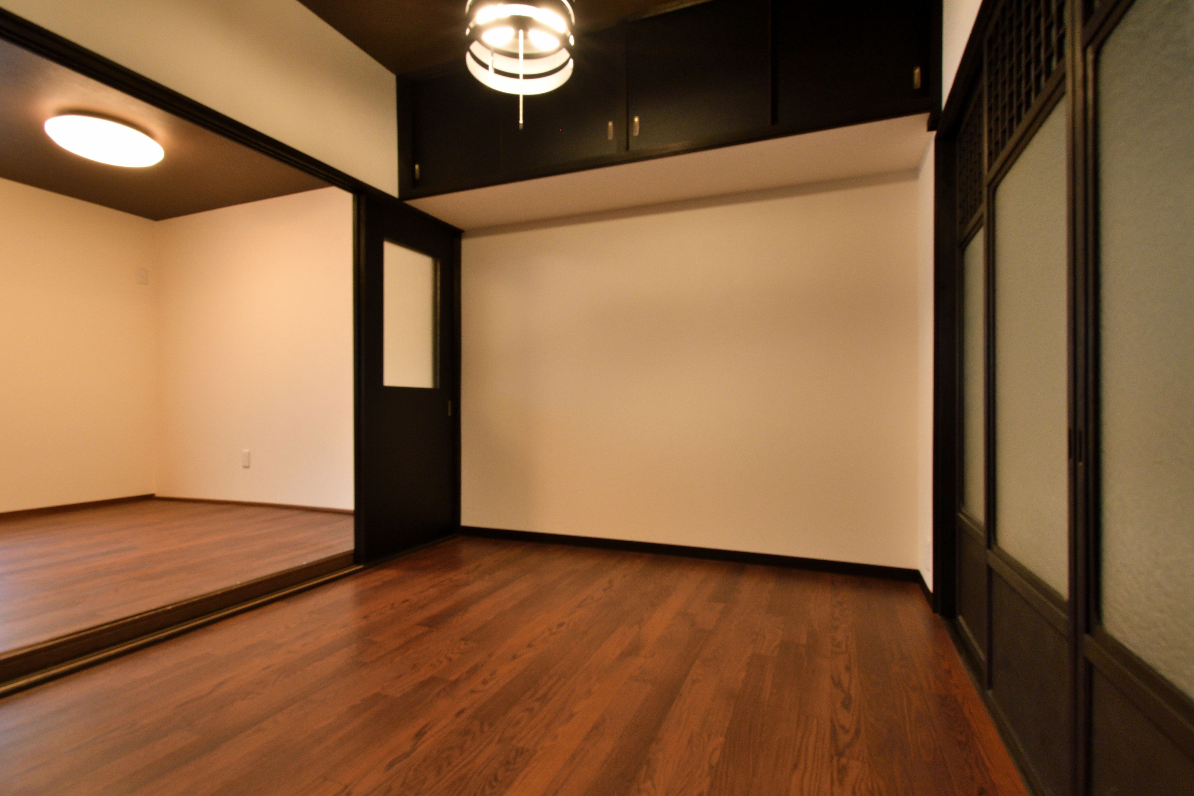 A room with wooden flooring, a black door, and a ceiling light fixture.