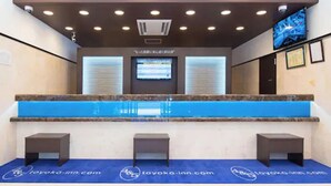 Un comptoir d’accueil surmonté d’une enseigne indiquant « ACCUEIL », un écran numérique et un tapis bleu orné de logos.