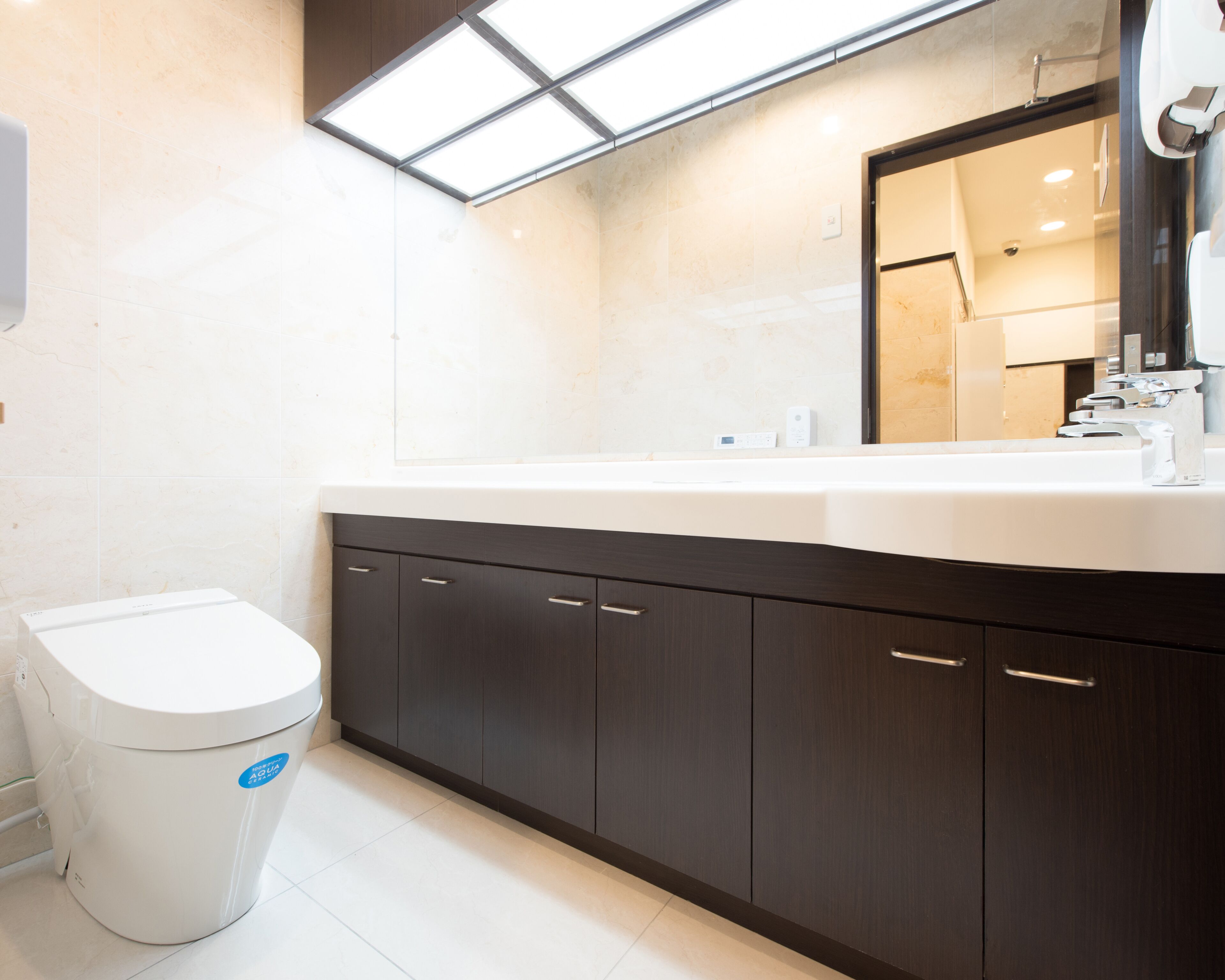 A modern bathroom with a white toilet, dark wooden cabinets, and a large mirror above the sink.
