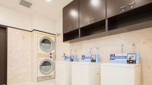 Une buanderie équipée de quatre machines à laver et d’un sèche-linge, chacun doté d’un panneau de commande.