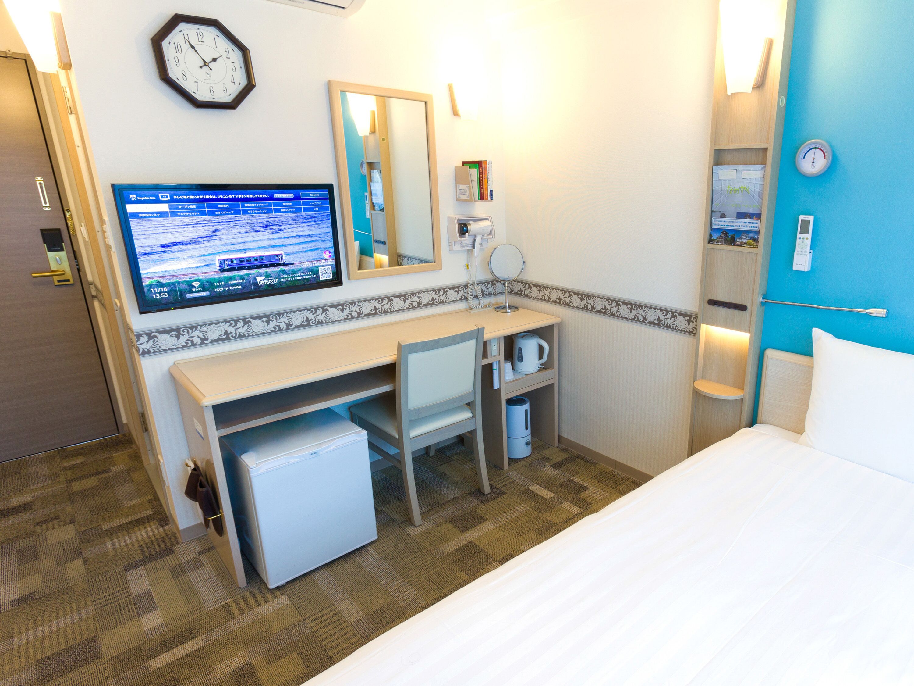 A hotel room with a bed, desk, chair, and a television displaying a travel website.