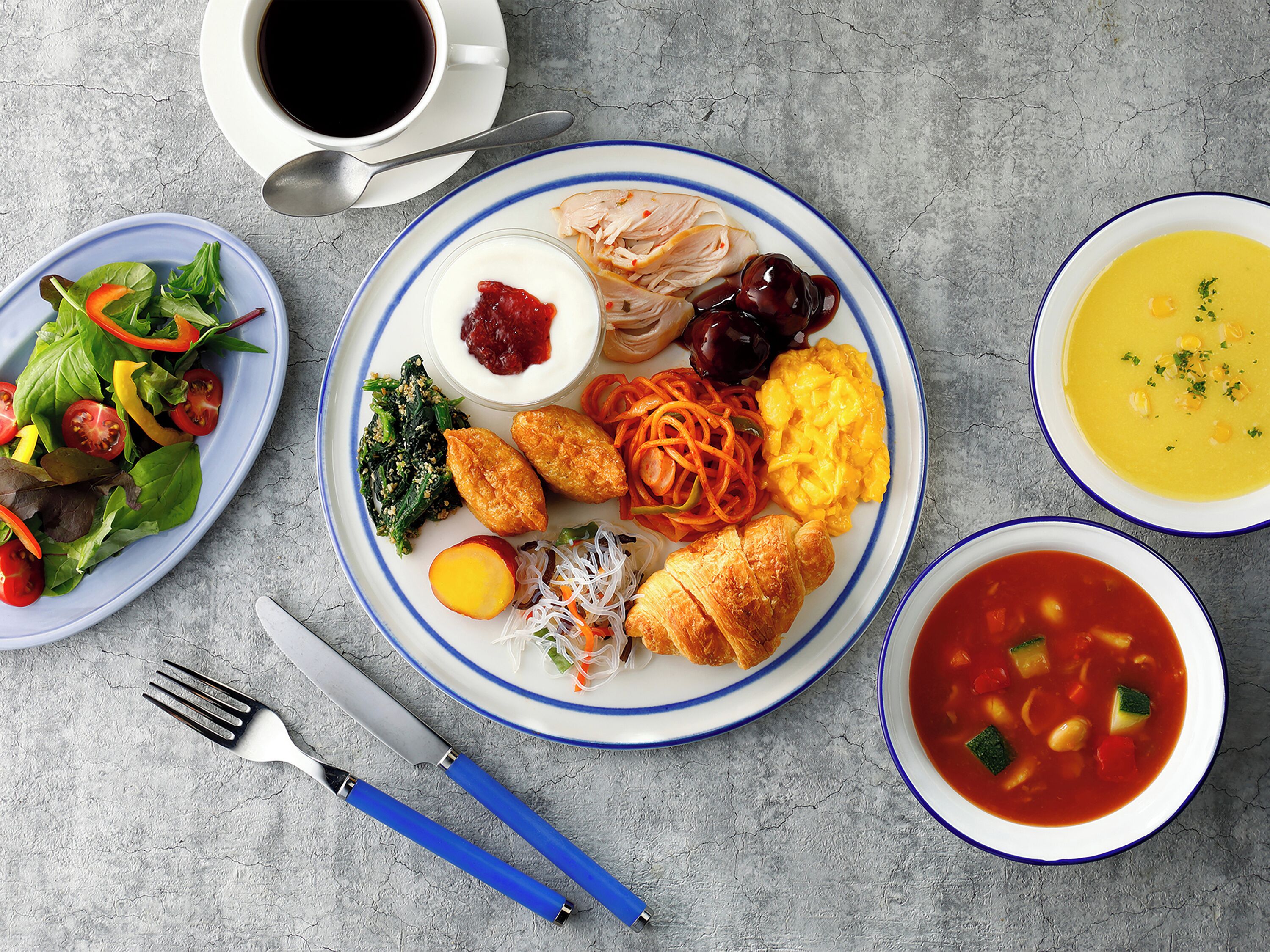A table with various dishes including a salad, a plate with eggs, vegetables, and a bowl of soup.