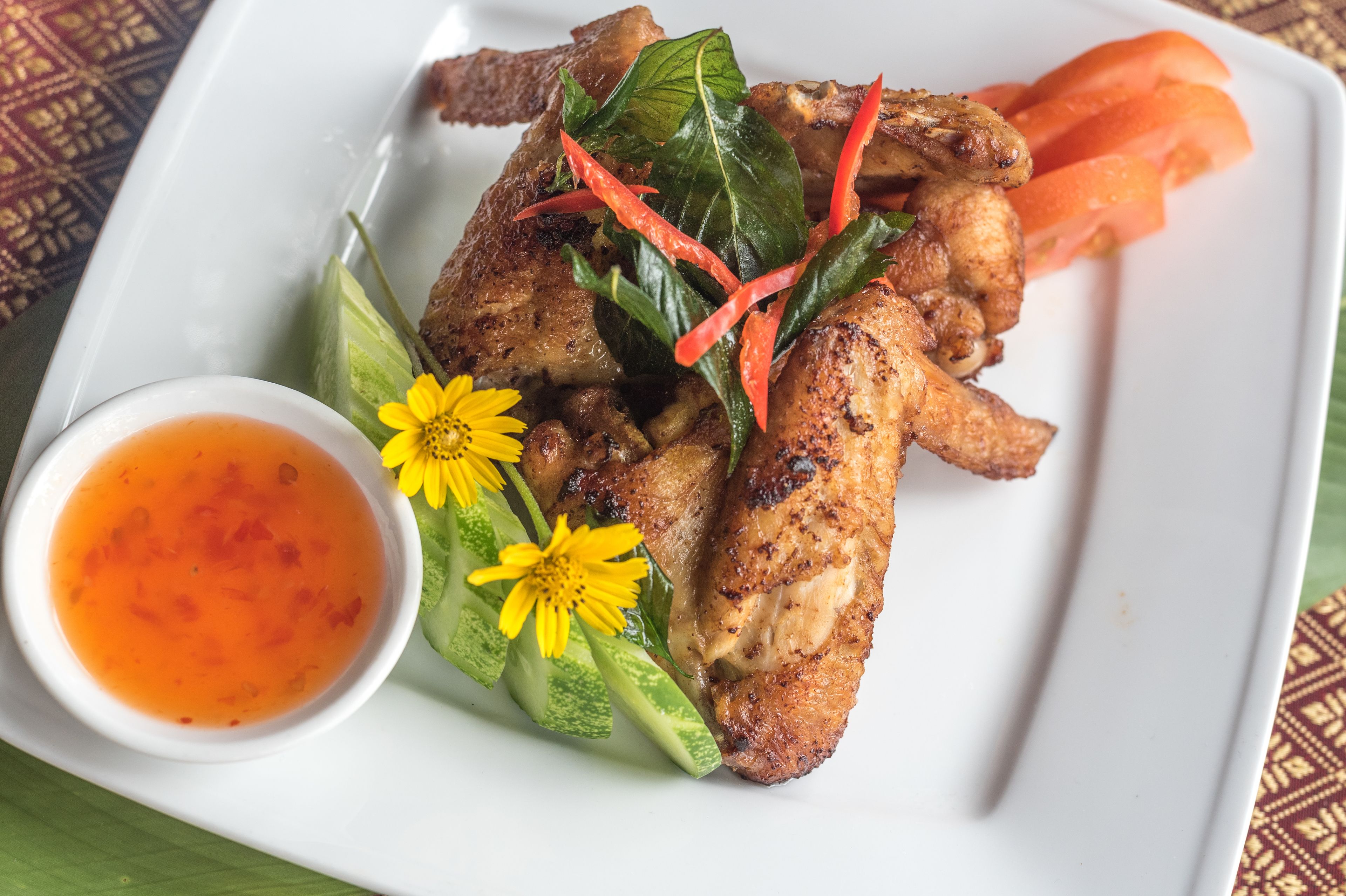 A plate of grilled chicken with vegetables and a small bowl of sauce.