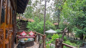 Une terrasse en bois avec un banc et une table, entourée d’une végétation luxuriante et d’une clôture rustique.