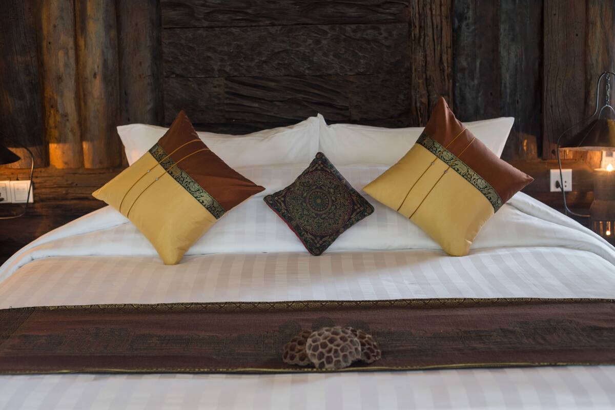 Una cama con ropa de cama blanca, dos almohadas decorativas y un cabecero de madera.