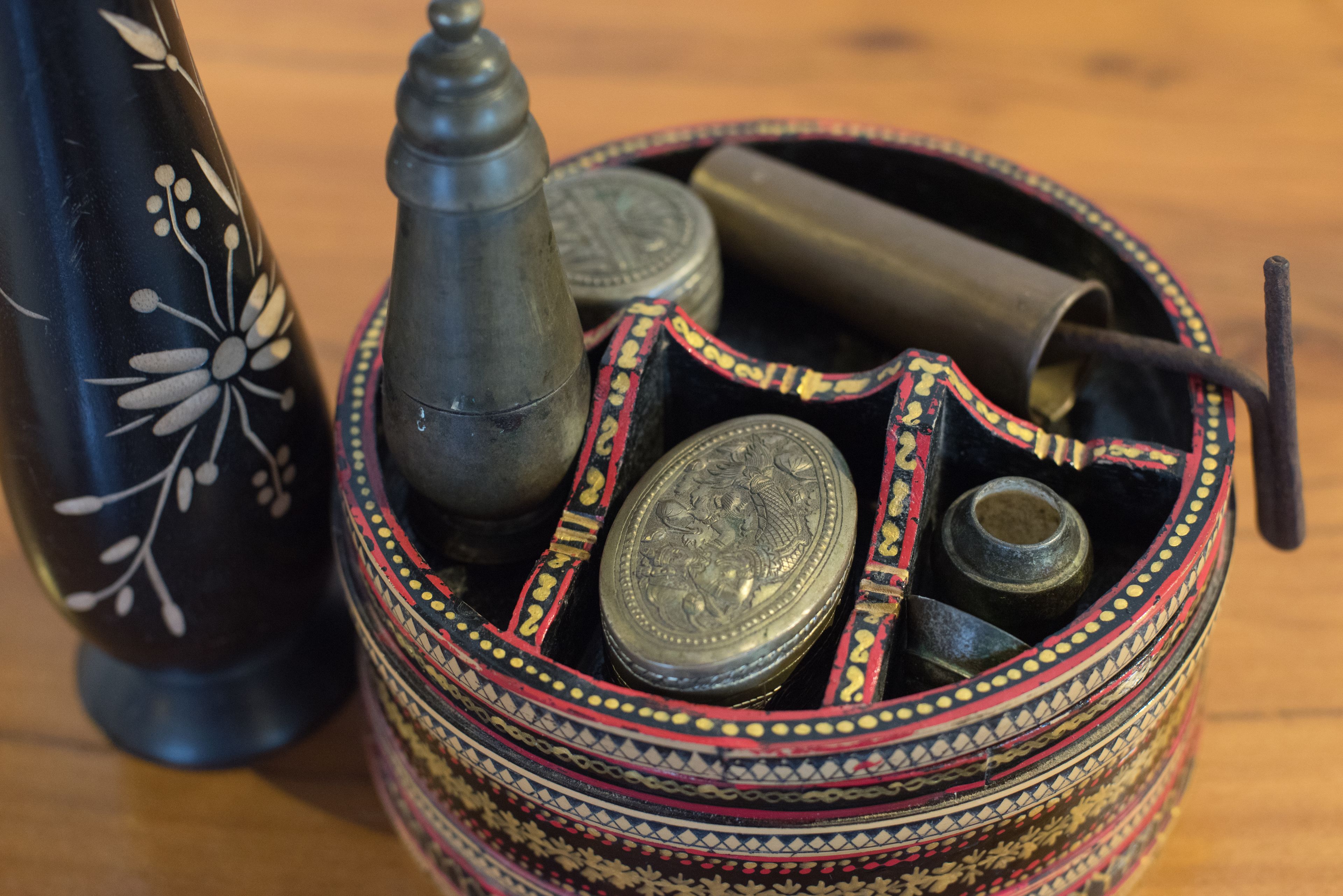 Un recipiente decorativo con diseños intrincados y objetos metálicos, como una botella y un contenedor cilíndrico.