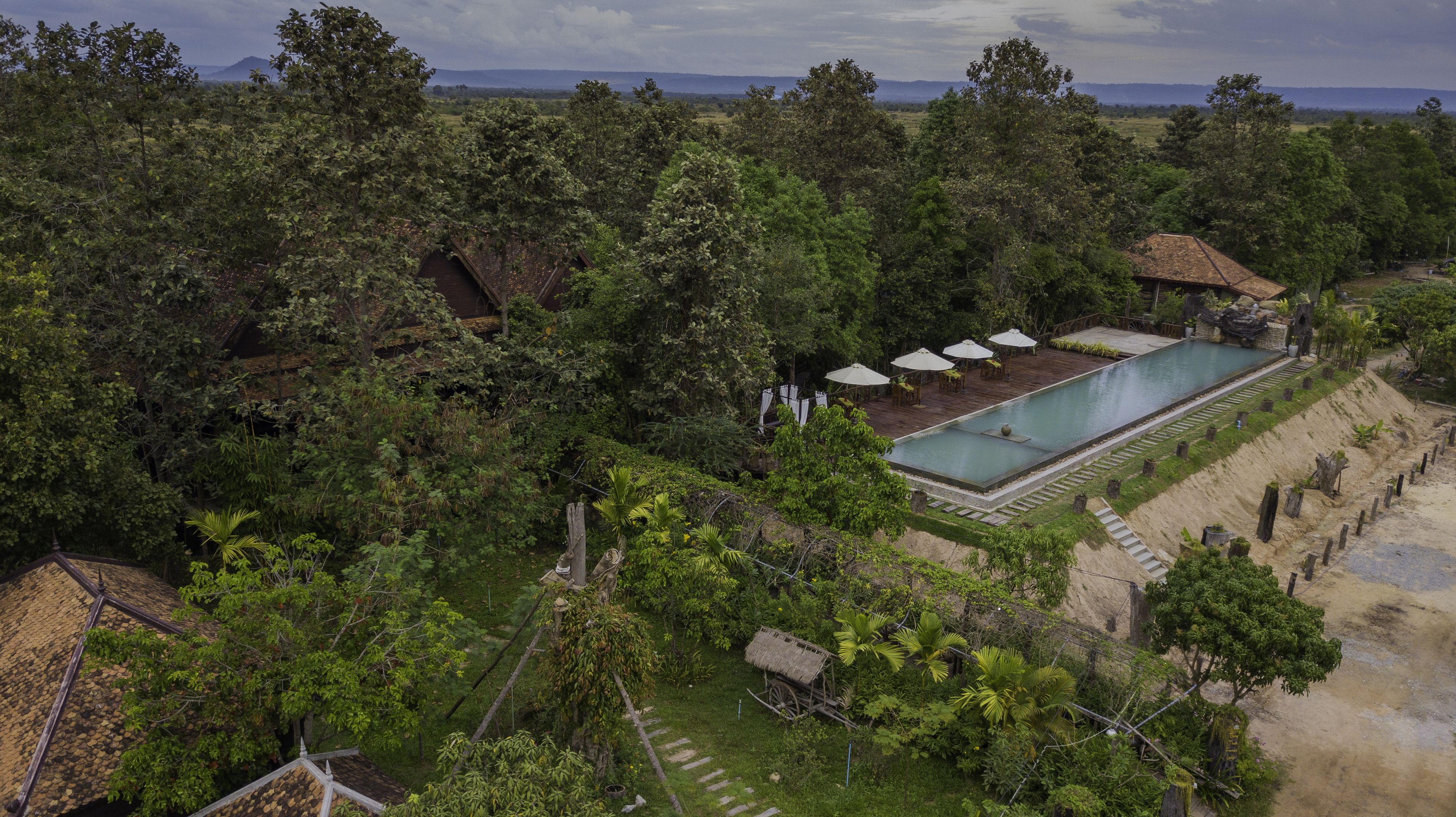 A resort with a swimming pool surrounded by lush greenery, a wooden deck, and a thatched-roof structure.