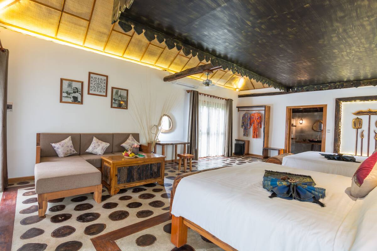 Una habitación amplia con una cama grande, un sofá, una mesa de centro de madera y un ventilador de techo.
