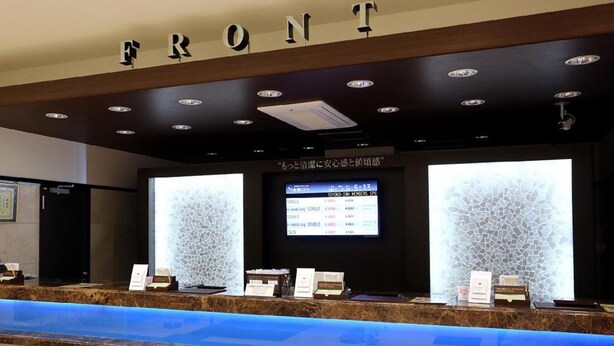 A reception area with a marble counter, a digital screen displaying room rates, and a sign above reading "FRONT".
