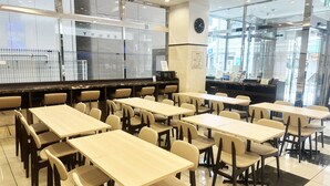 Un espace repas moderne avec plusieurs tables et chaises, une horloge au mur et un comptoir où est affiché le menu.