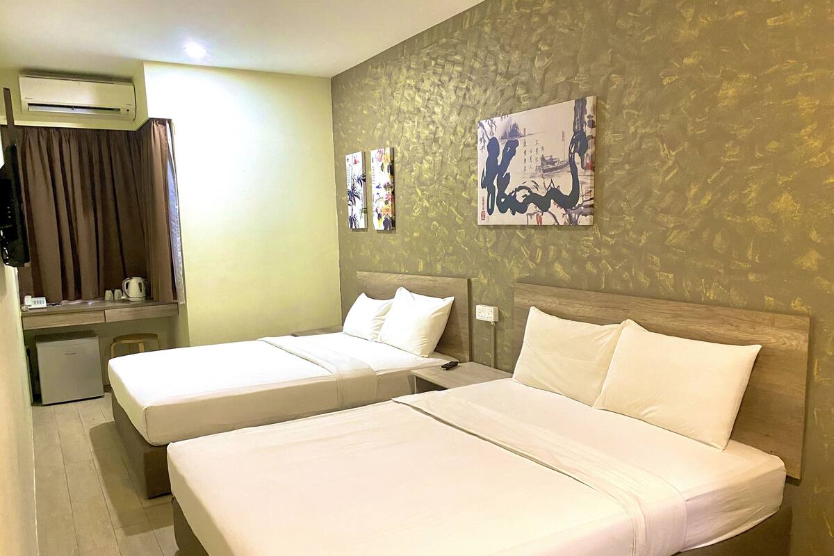 Une chambre d’hôtel avec deux lits, un bureau, un réfrigérateur et un mur décoré d’œuvres d’art.