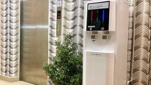 Un distributeur d’eau doté d’un écran numérique, une plante en pot et une porte d’ascenseur métallique.