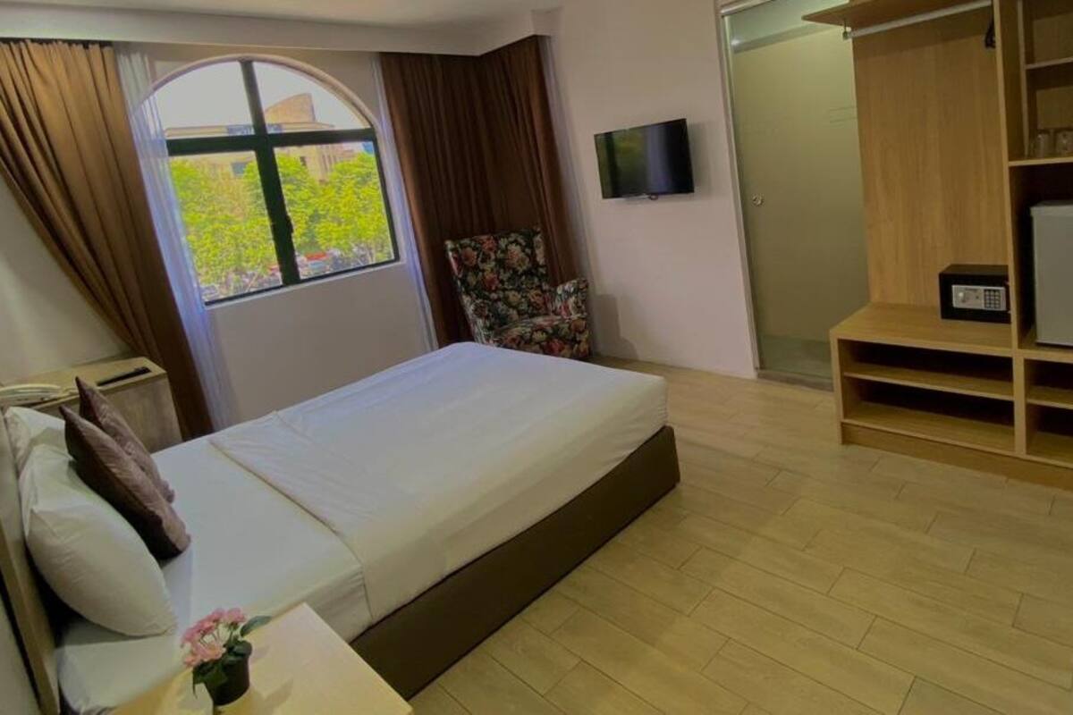 Une chambre d’hôtel avec un lit, un téléviseur fixé au mur, une armoire et une petite table sur laquelle est posé un vase de fleurs.