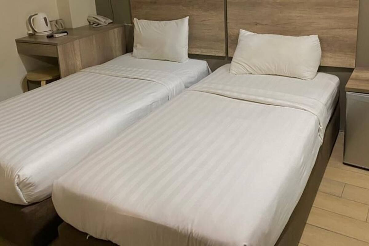 Une chambre double avec deux lits, une table de chevet avec un téléphone et une bouilloire, et un petit placard.