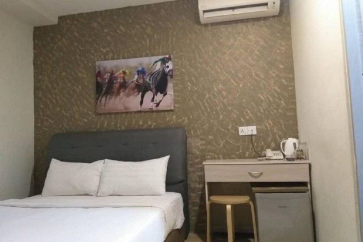 Een hotelkamer met een bed, een bureau met stoel, een kleine koelkast en een airconditioning.
