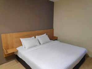 Un lit bien fait, avec une tête de lit en bois, une table de chevet et une étagère fixée au mur.