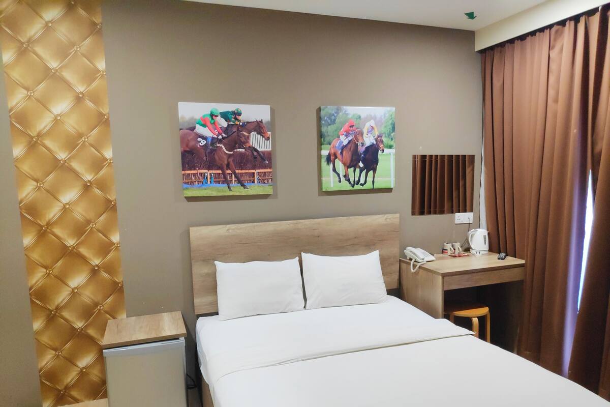 Une chambre d’hôtel avec un lit, un bureau, une chaise, un petit réfrigérateur et deux tableaux au mur.
