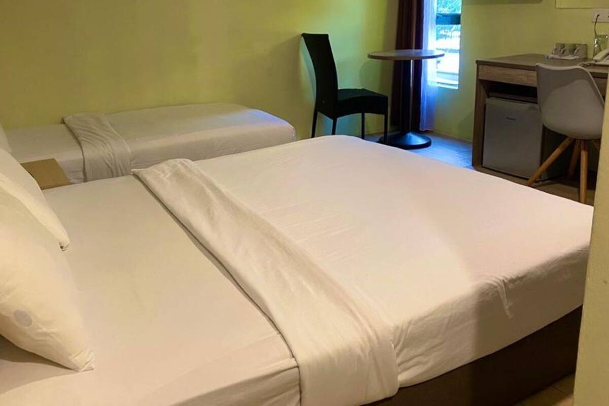 Une chambre avec deux lits simples, un petit bureau avec une chaise et une fenêtre avec des rideaux.