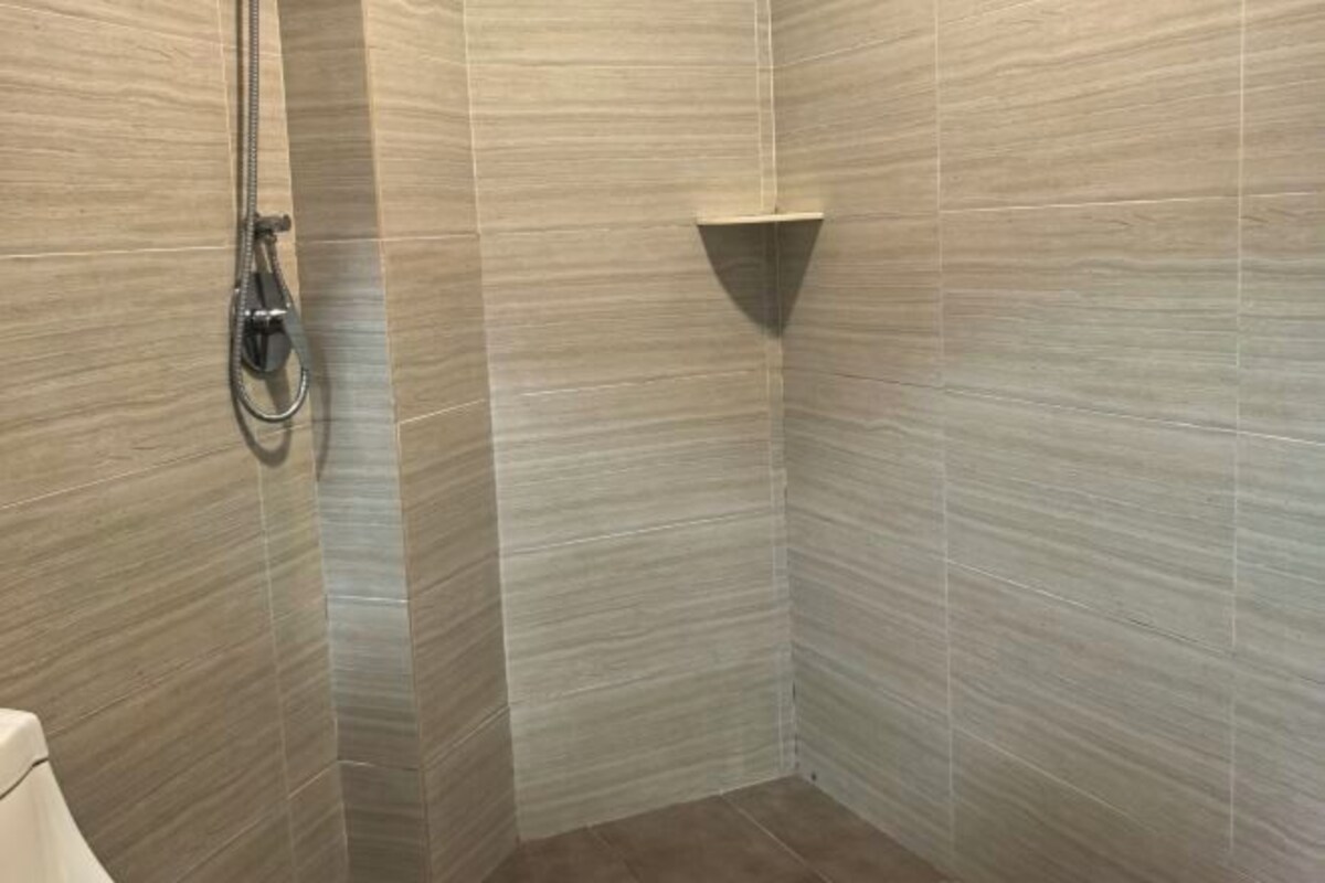 Een douchegedeelte met een handdouche en een hoekplankje.