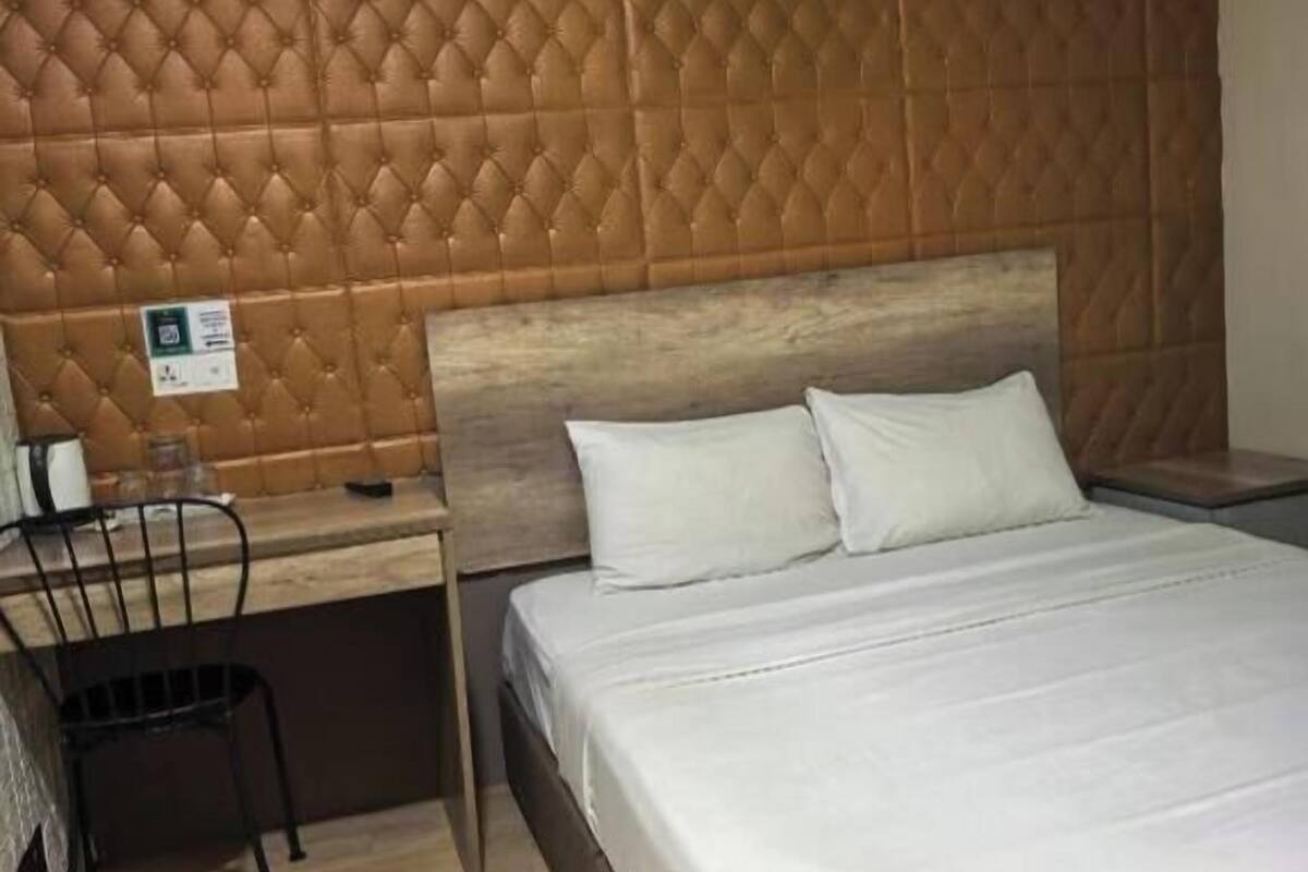 Un lit standard de taille « queen », doté d’une tête de lit ornée d’un motif en losanges, d’un bureau en bois, d’une chaise et d’un panneau indiquant l’absence de fenêtre.