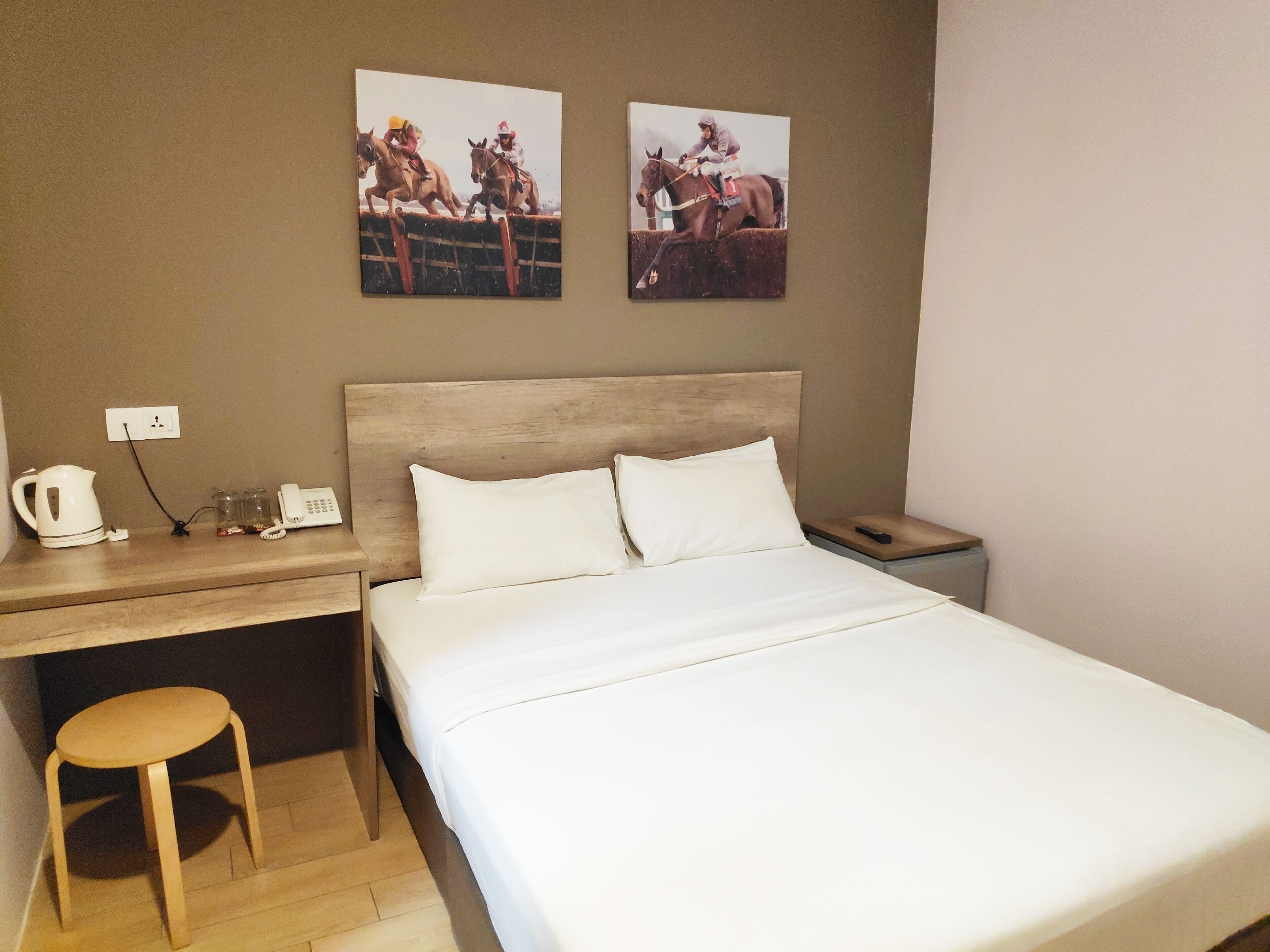 A hotel room with a bed, a wooden desk, a chair, a telephone, and two framed pictures on the wall.