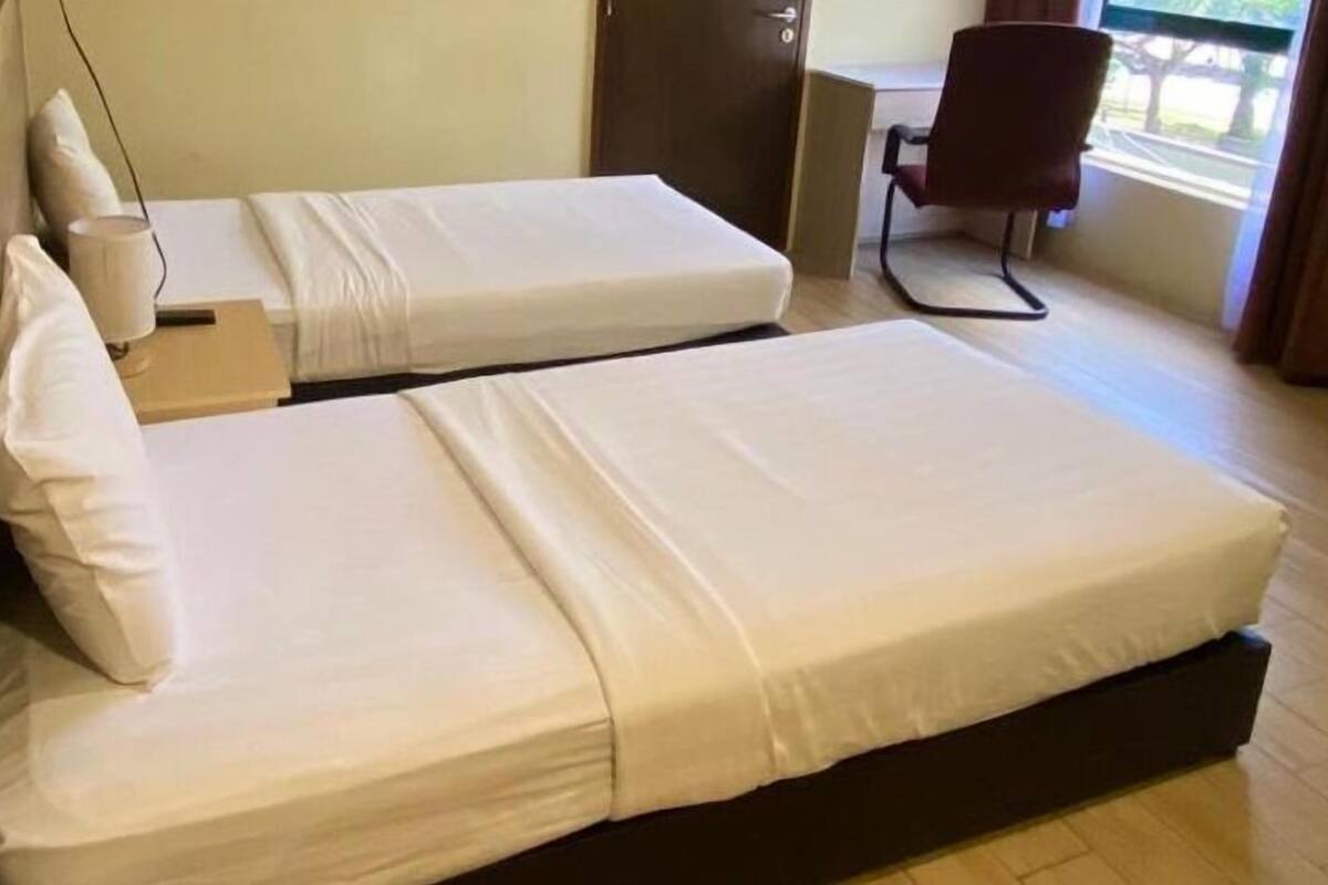 Une chambre d’hôtel avec deux lits simples, un bureau avec une chaise et une fenêtre donnant sur un paysage agréable.