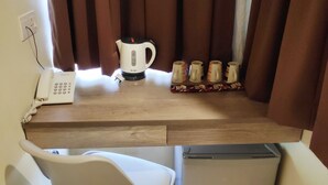 Une cuisine compacte équipée d’une cuisinière intégrée, d’un petit réfrigérateur, d’une chaise blanche, d’une machine à café et d’un téléphone posé sur le comptoir.