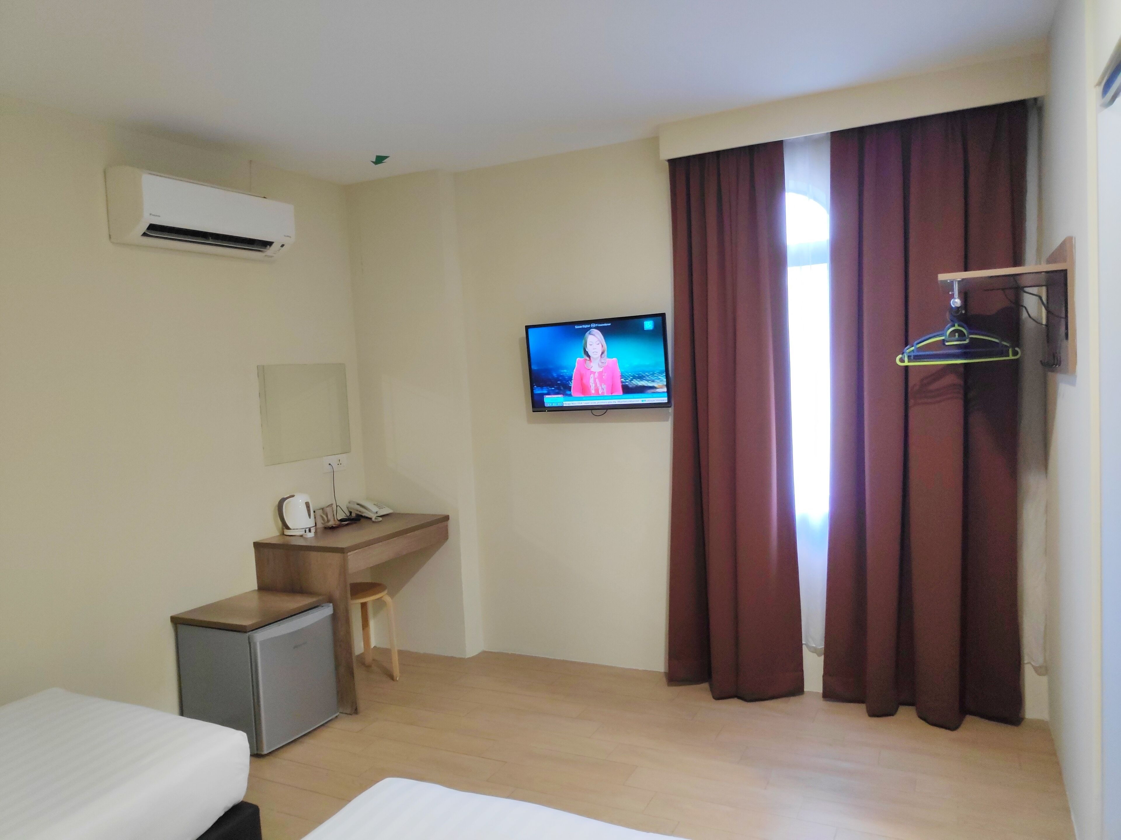 A hotel room with a bed, a desk with a chair, a television, an air conditioner, and a wardrobe.