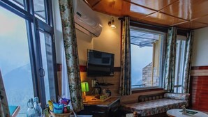 A cozy room with wooden flooring, a wooden dining table with chairs, a sofa, a small round table, and a TV. - Udechee Huts Hotel (Dharamshala)