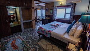 A bedroom with a bed, bedside table, lamp, and a desk with a chair. - Udechee Huts Hotel (Dharamshala)