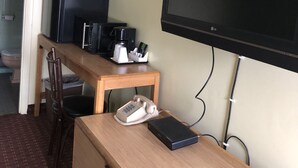 Habitación de hotel compacta con un escritorio de madera, un refrigerador negro, cafetera, teléfono y un televisor de pantalla plana grande montado en la pared.