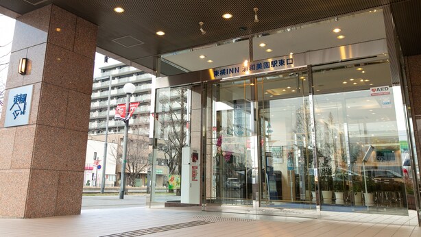The entrance of a hotel with a modern design, featuring a glass facade and a sign indicating it is an INN. - Toyoko Inn Urawa Misono Station (Saitama)
