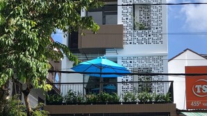 A modern building with a balcony, a blue umbrella, and a menu board. - La An Homestay (Da Nang)