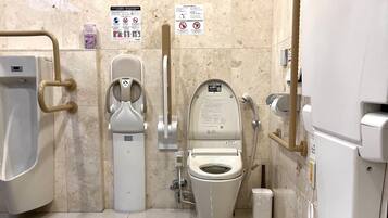 Des toilettes pour hommes comprenant un urinoir, des toilettes équipées d’un siège-bidet et un distributeur de gel hydroalcoolique.
