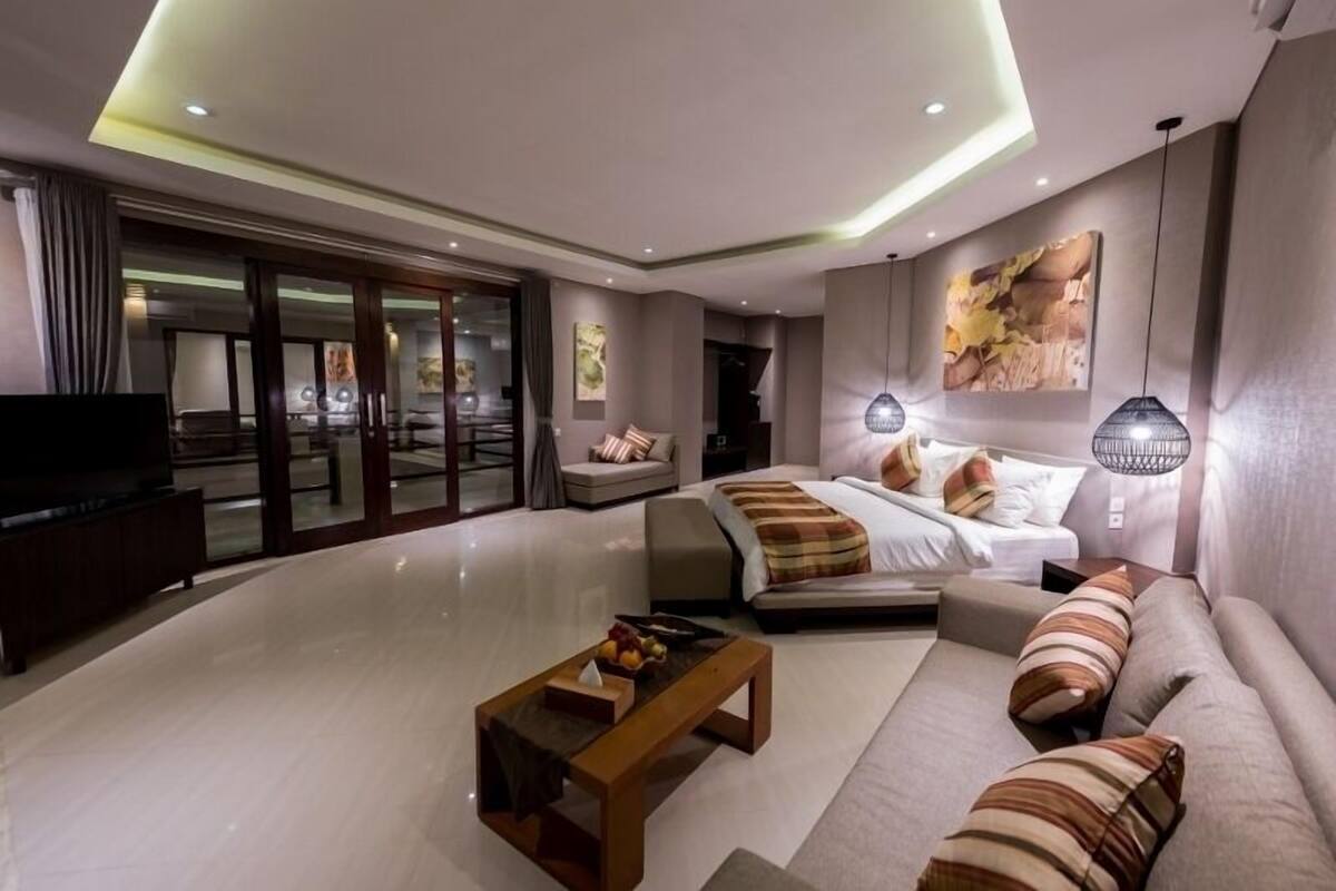A modern hotel room with a large bed, a sofa, a coffee table, and a TV.