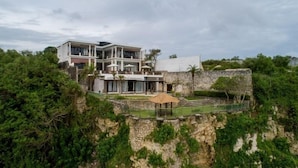 A modern two-story house with a large balcony, a swimming pool, and lush greenery surrounding the property. - Villa Maiara (Ungasan)